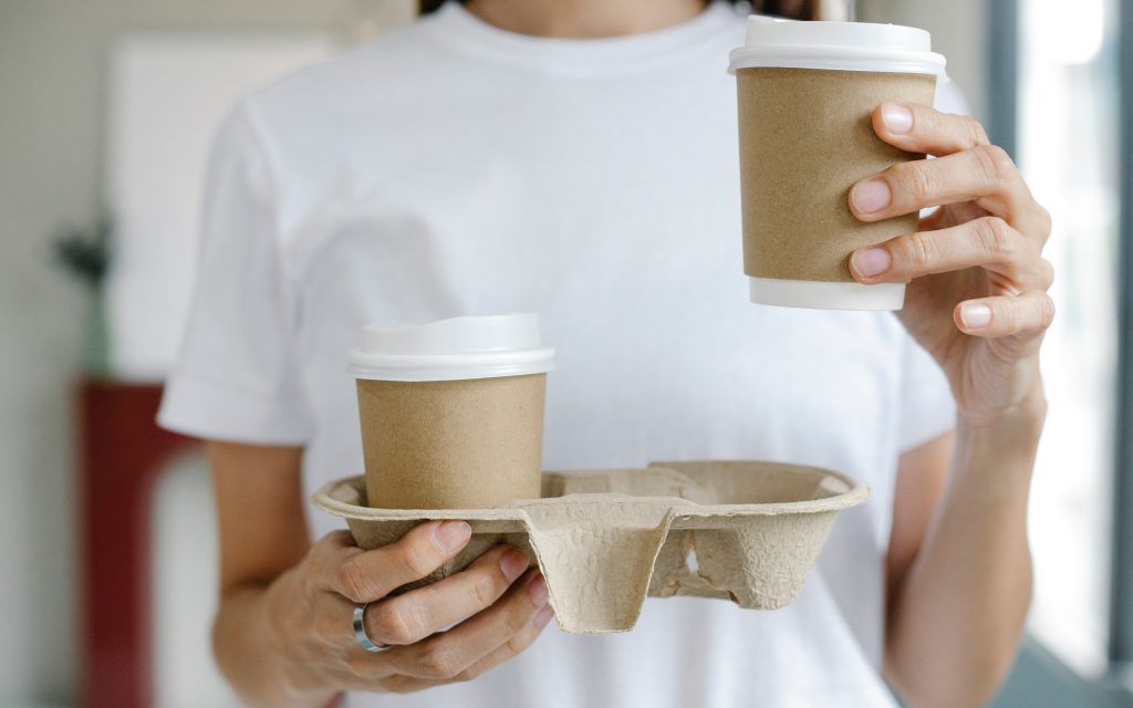 Une femme tient un plateau et deux cafés à emporter.
