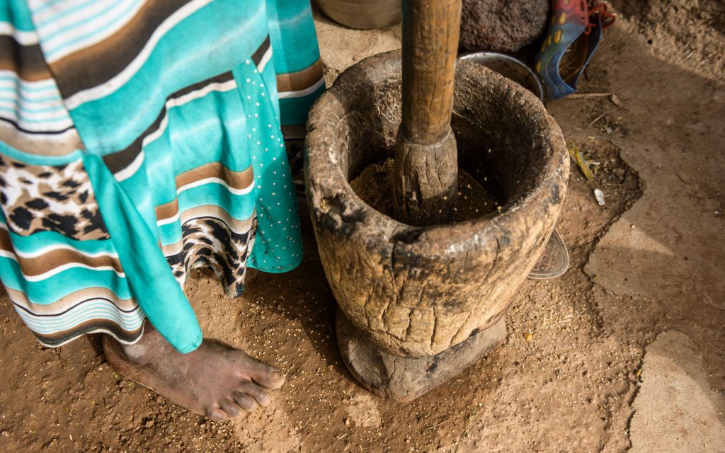 Une femme moud des grains de café dans un grand pilon et un mortier.