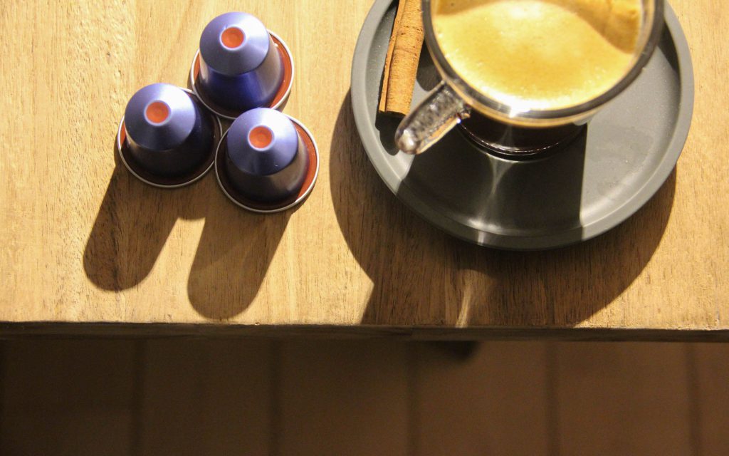 Capsules de café en aluminium à côté d'une tasse de café.