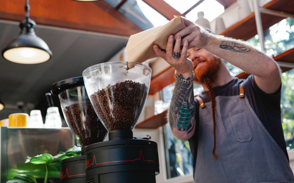 Un barista remplit la trémie d'un moulin avec des grains de café torréfiés.