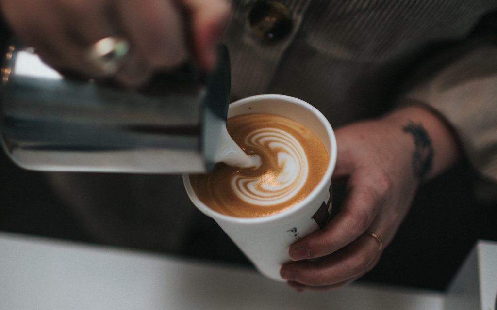 Un barista verse du lait dans le café pour créer un latte art.