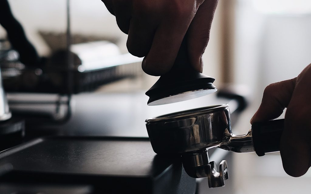 Un barista tasse du café moulu dans un portafiltre.